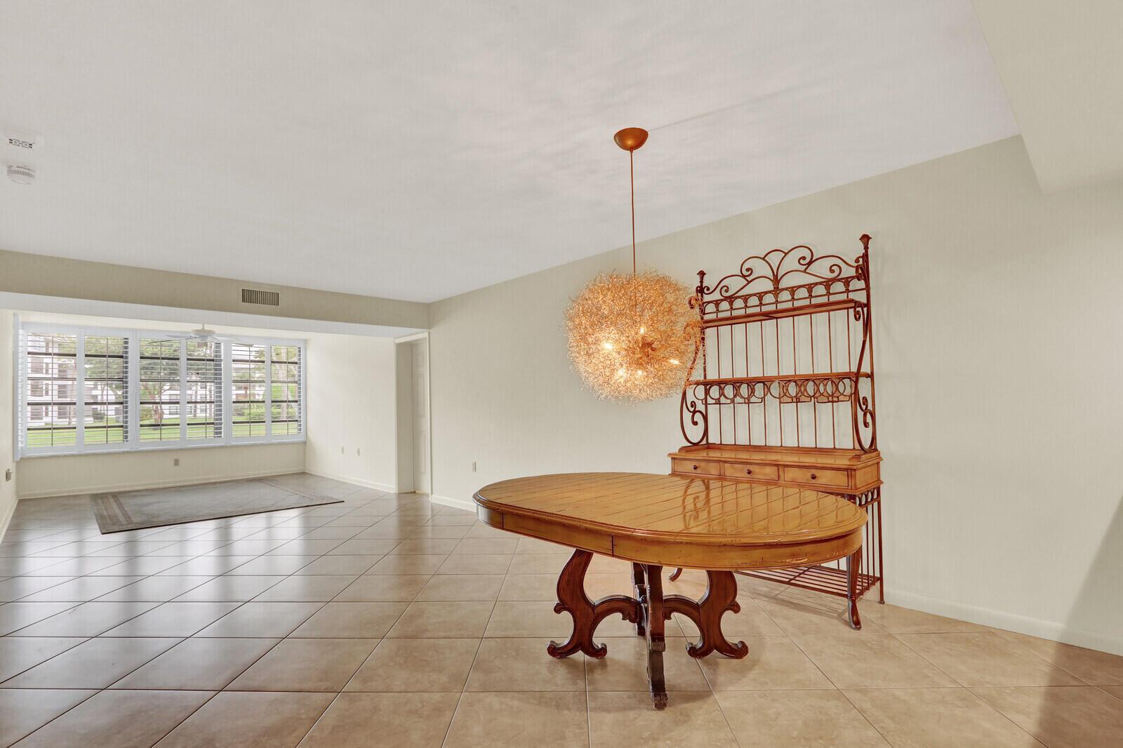 A dining area with tile floors, a wooden table, a metal hutch, and a pendant light — 3636 WHITEHALL Drive # 105, West Palm Beach FL 33401, WEST PALM BEACH, FL