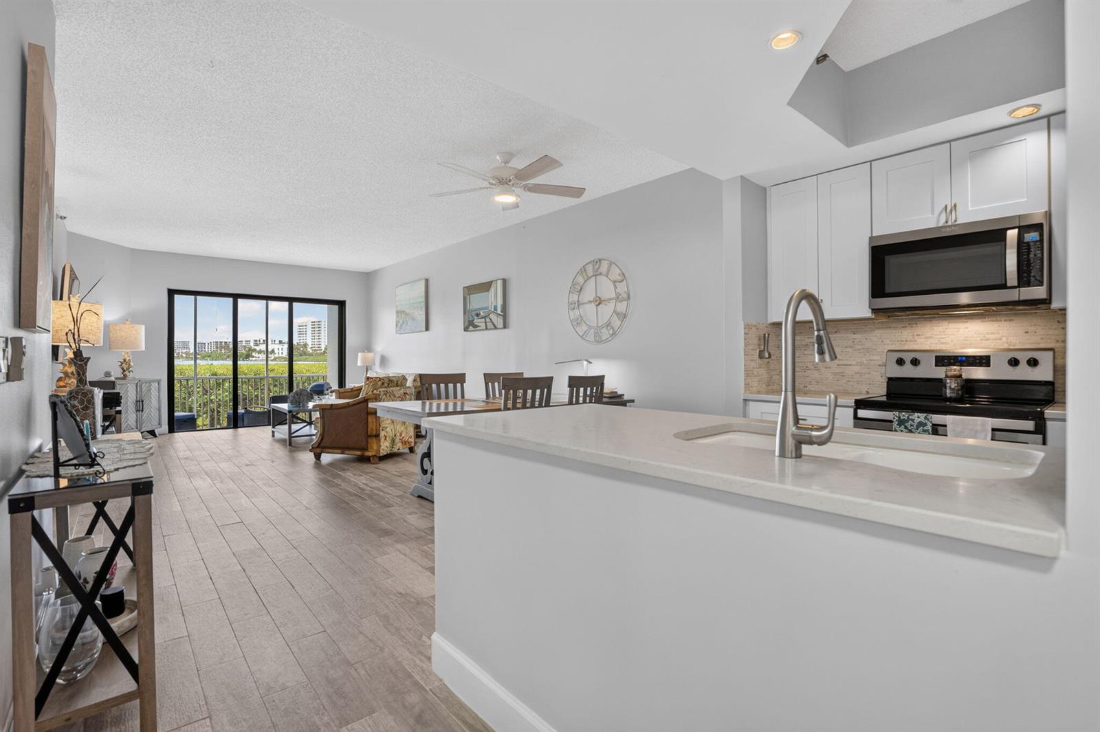 A kitchen with white cabinets and a quartz island overlooks an open-concept living and dining area — 200 Waterway Road # 104, Tequesta FL 33469, TEQUESTA, FL