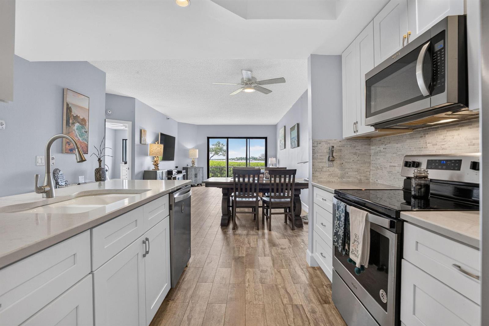 A kitchen with white cabinets and stainless steel appliances opens into a dining area — 200 Waterway Road # 104, Tequesta FL 33469, TEQUESTA, FL