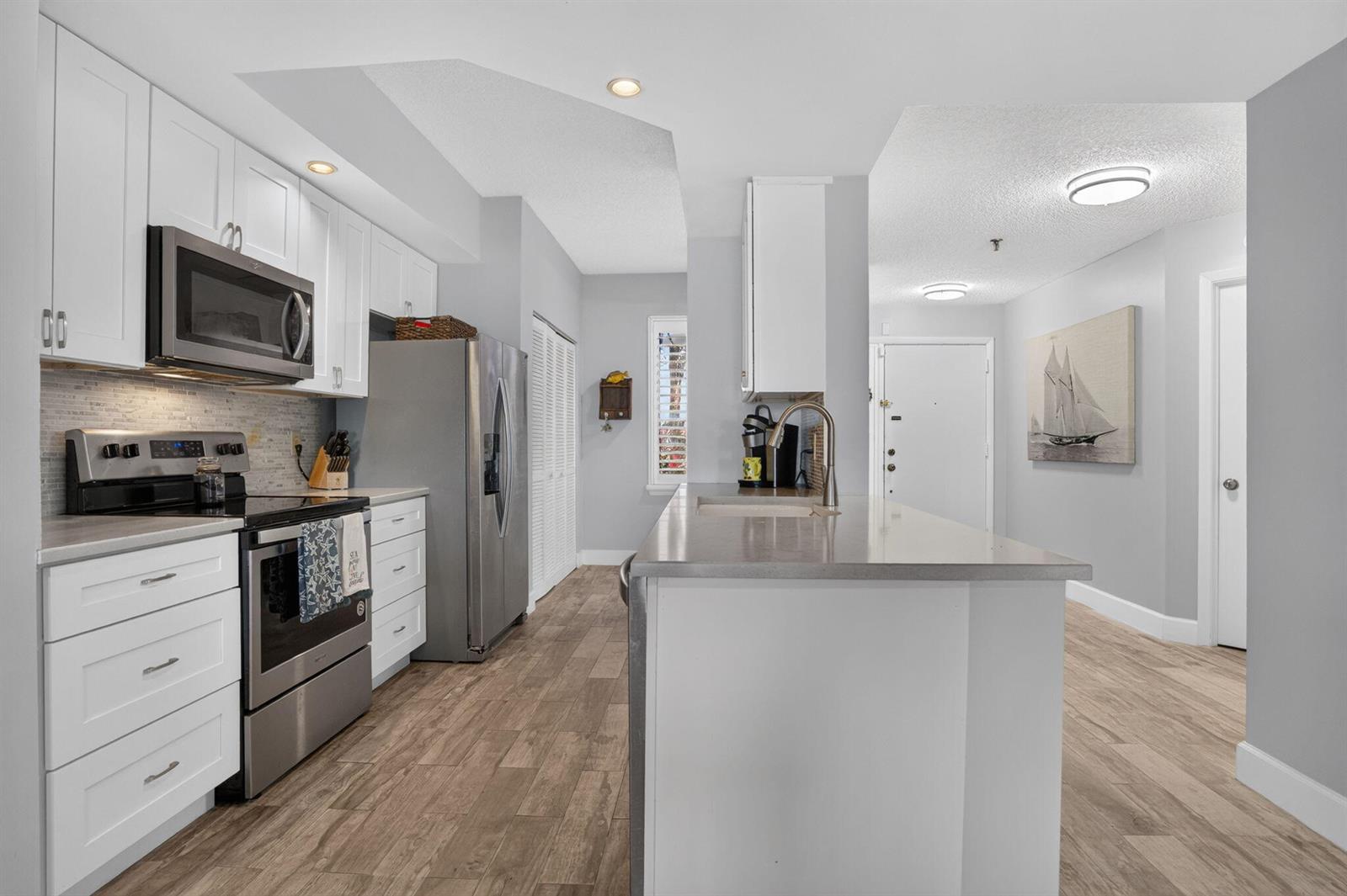 A modern kitchen features white cabinetry, stainless steel appliances, a center island, and wood-look flooring — 200 Waterway Road # 104, Tequesta FL 33469, TEQUESTA, FL