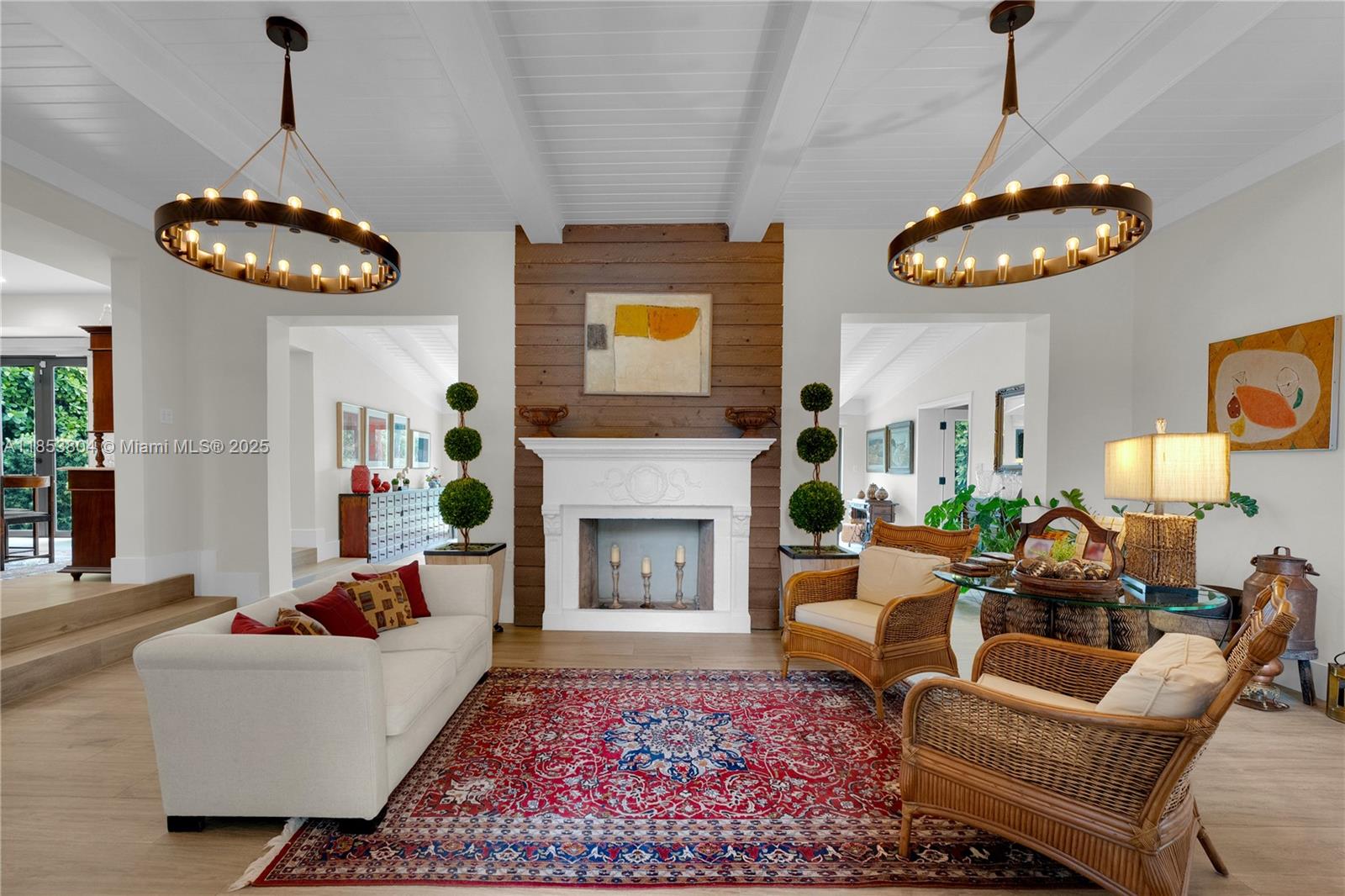 A living room features a white fireplace, wood-paneled accent wall, two chandeliers, and wicker furniture — 4475 N Meridian Ave, Miami Beach FL 33140, MIAMI BEACH, FL