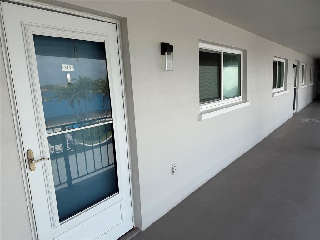 A white exterior door with a glass storm door leads to a concrete walkway — 649 TAMIAMI TRAIL S UNIT 310, VENICE, FL