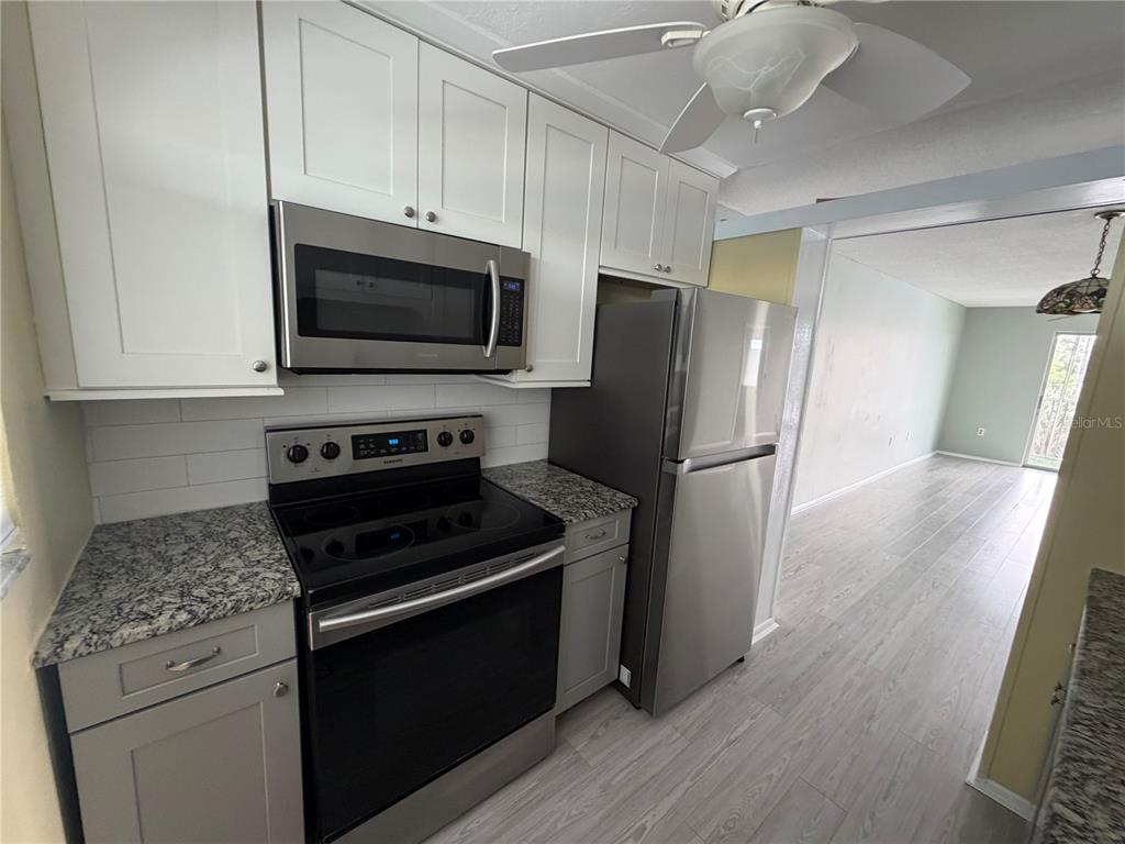 A kitchen features white upper cabinets, gray lower cabinets, granite countertops, and stainless steel appliances — 649 TAMIAMI TRAIL S UNIT 310, VENICE, FL