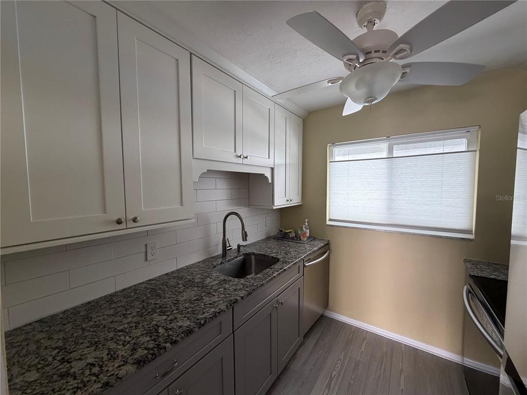 A kitchen features white upper cabinets, gray lower cabinets, granite countertops, and a subway tile backsplash — 649 TAMIAMI TRAIL S UNIT 310, VENICE, FL