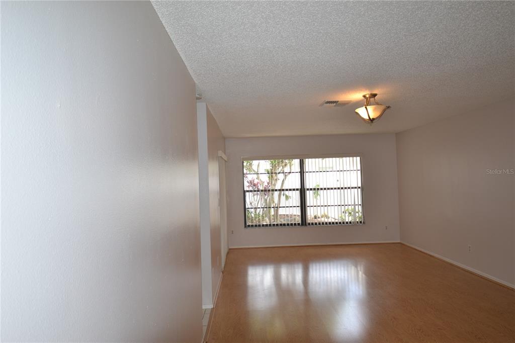 An empty room with light wood-look flooring, a textured ceiling, and a large window — 2001 DOVER COURT, OLDSMAR, FL