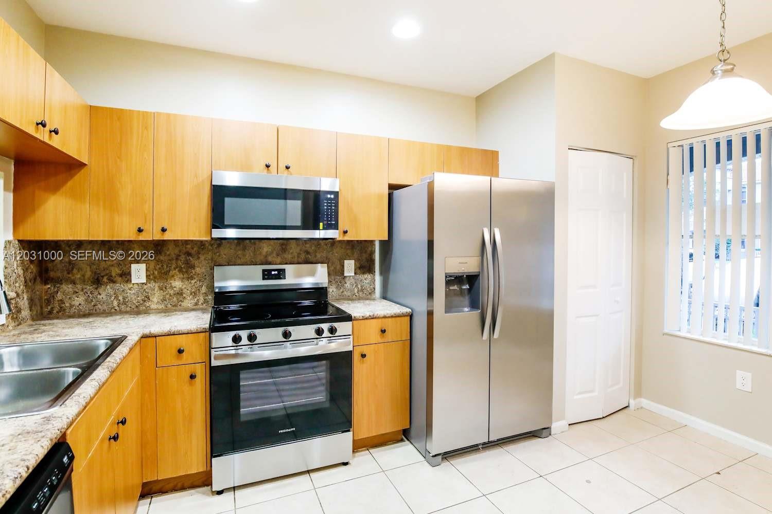 A kitchen features light wood cabinets, stainless steel appliances, and a tiled floor — MIRAMAR, FL