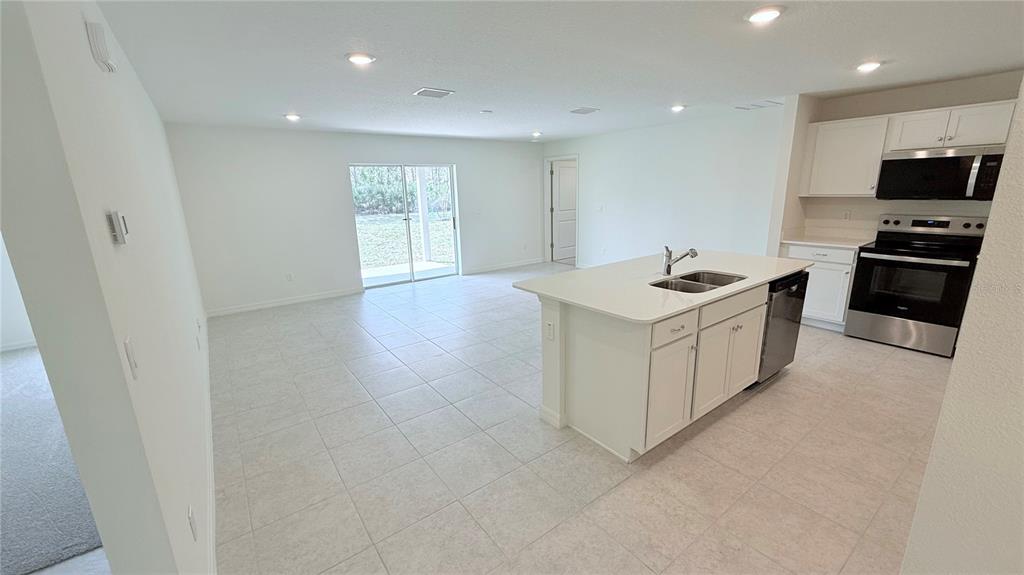 A bright kitchen with a white island and stainless steel appliances opens to a living area — 52 PRINCETON LANE, PALM COAST, FL