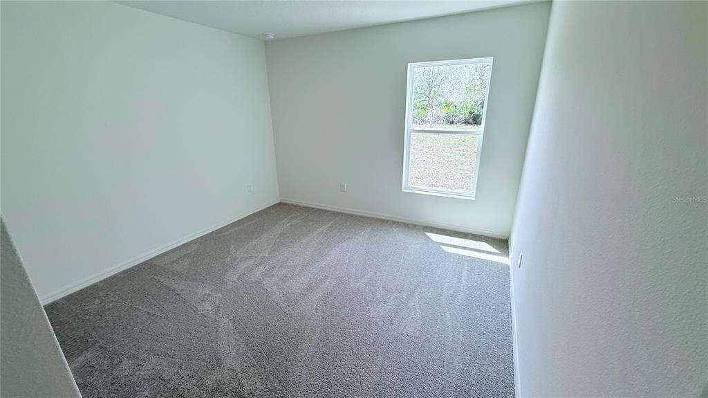 A bedroom with neutral walls, gray carpet, and a single window overlooking a grassy yard — 52 PRINCETON LANE, PALM COAST, FL