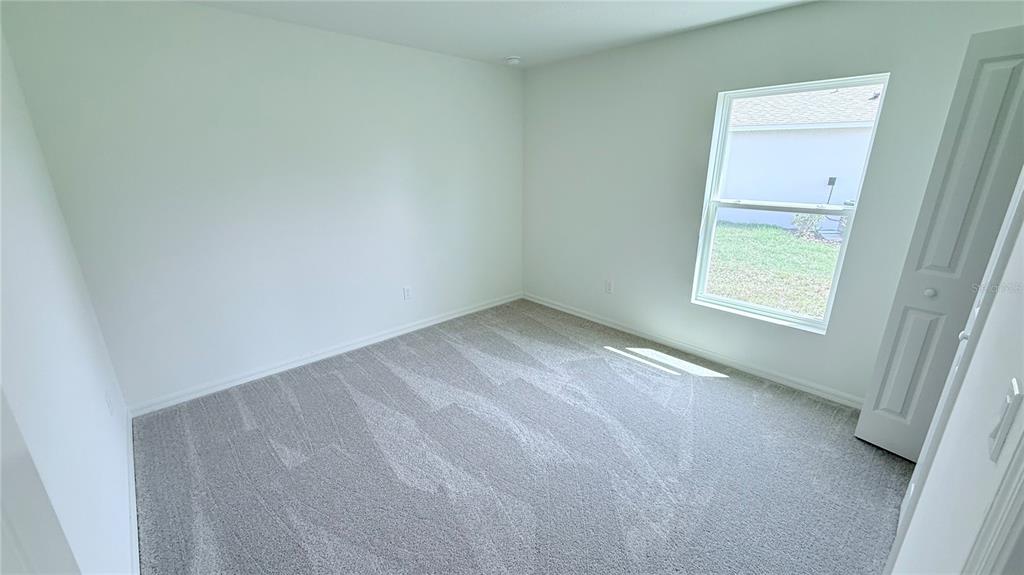 A bedroom with light gray carpet, white walls, and a window overlooking a grassy yard — 52 PRINCETON LANE, PALM COAST, FL