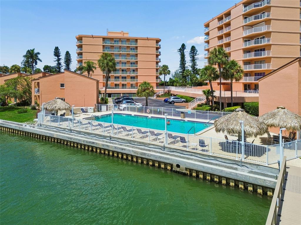 An outdoor swimming pool sits beside a canal, surrounded by multi-story apartment buildings and palm trees — 7430 SUNSHINE SKYWAY LANE S UNIT 201, ST PETERSBURG, FL