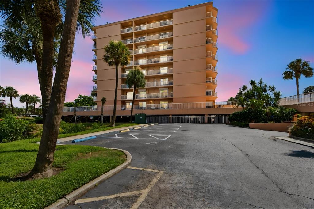 A multi-story tan apartment building stands behind an asphalt parking lot with palm trees — 7430 SUNSHINE SKYWAY LANE S UNIT 201, ST PETERSBURG, FL