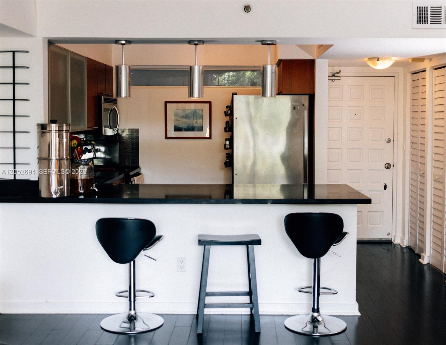 A kitchen features a black countertop breakfast bar with three stools and stainless steel appliances — 700 NE 63rd St # D205, Miami FL 33138, MIAMI, FL