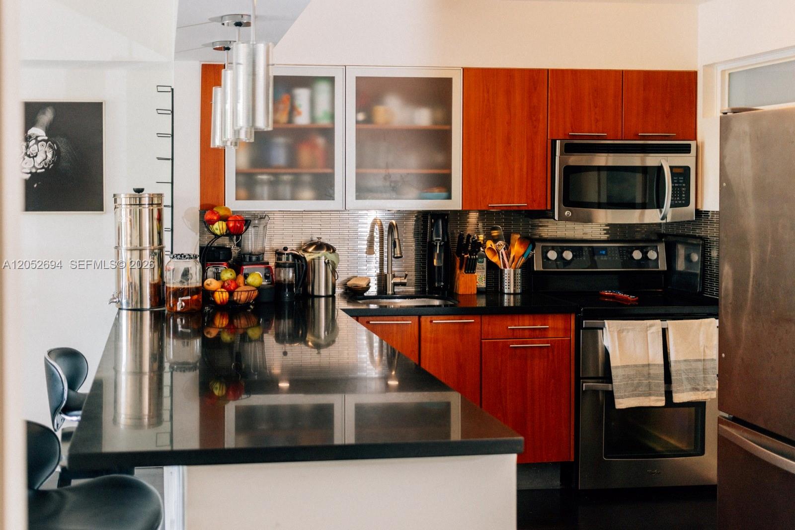 A kitchen features wood cabinets, black countertops, stainless steel appliances, and a breakfast bar — 700 NE 63rd St # D205, Miami FL 33138, MIAMI, FL