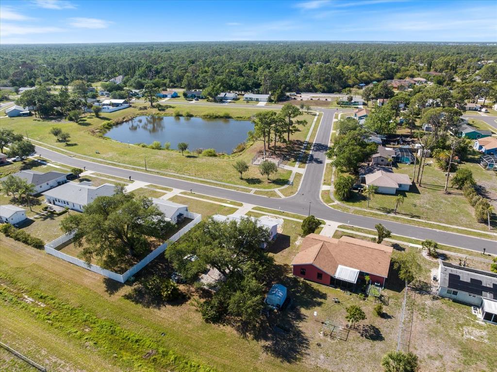 An aerial view shows a residential neighborhood with houses, a pond, and surrounding trees — 5494 GABO ROAD, NORTH PORT, FL