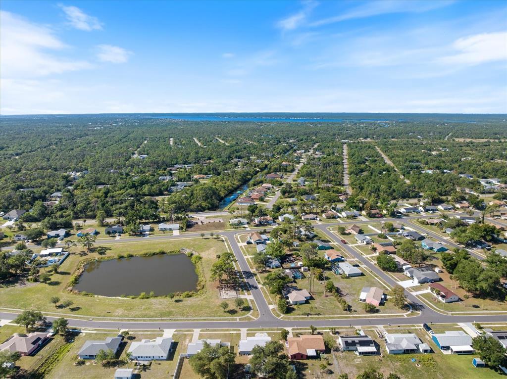 An aerial view shows a suburban neighborhood with a pond, houses, and surrounding wooded areas — 5494 GABO ROAD, NORTH PORT, FL