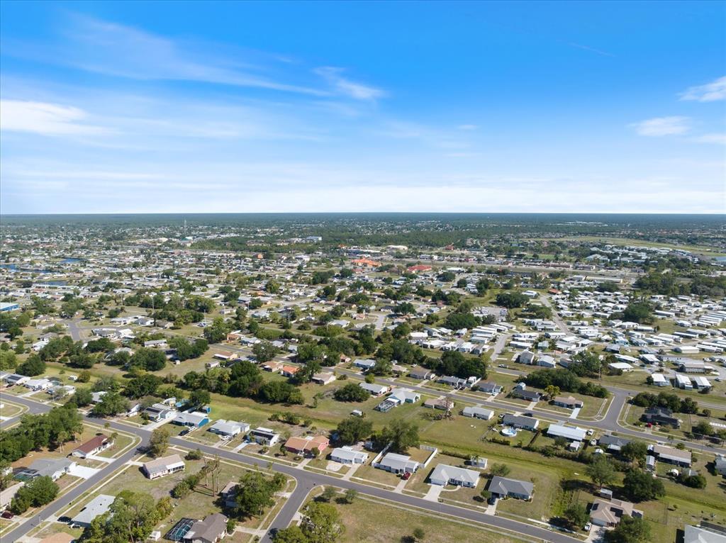 An aerial view shows a residential neighborhood with many houses and streets under a blue sky — 5494 GABO ROAD, NORTH PORT, FL