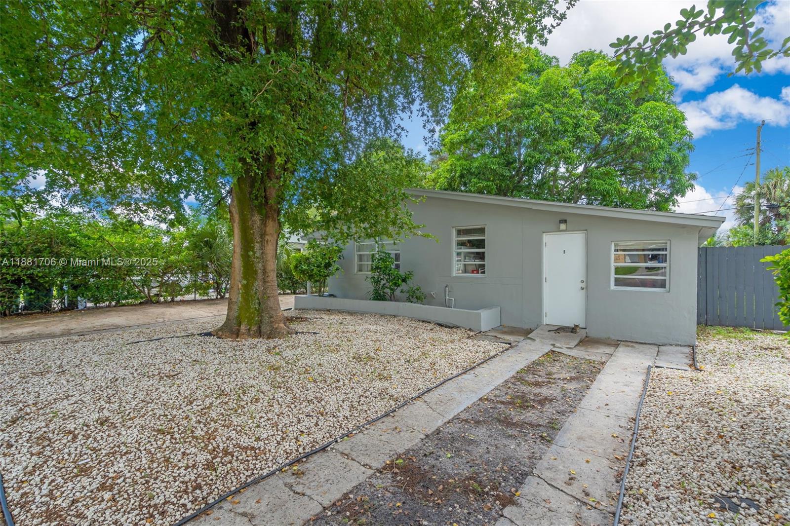 A gray, single-story house features a gravel yard, a large tree, and a concrete walkway — 3380 NW 8th Pl, Lauderhill FL 33311, LAUDERHILL, FL