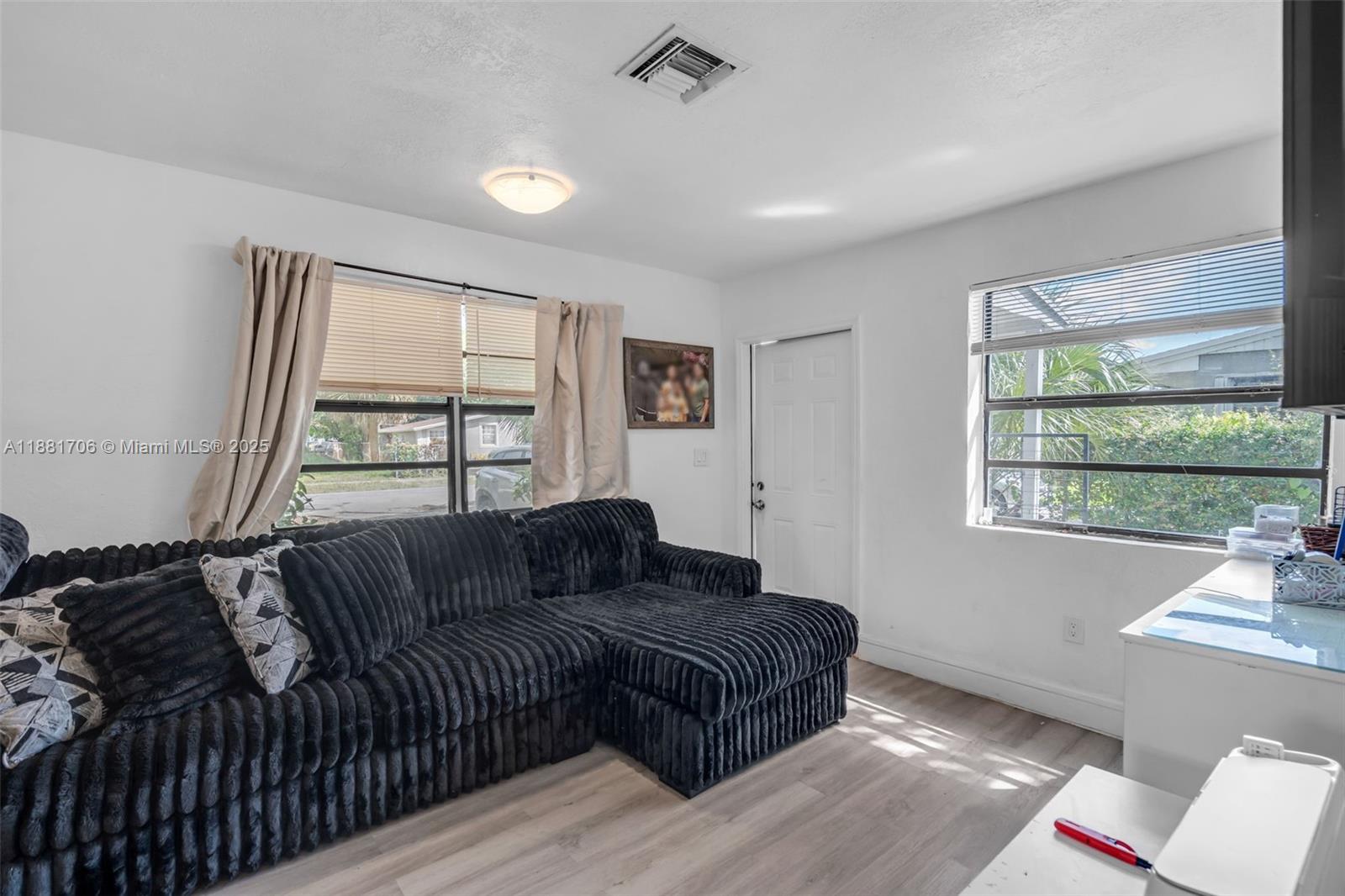 A living room features a black sectional sofa, light wood flooring, and two windows — 3380 NW 8th Pl, Lauderhill FL 33311, LAUDERHILL, FL