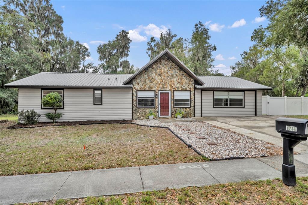 A single-story house with a stone-accented front entrance, light siding, and a metal roof — 1240 W VOORHIS AVENUE, DELAND, FL