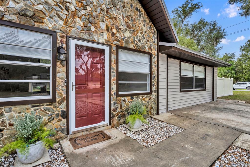 A stone-front house exterior features a red front door, white trim, and a concrete walkway — 1240 W VOORHIS AVENUE, DELAND, FL