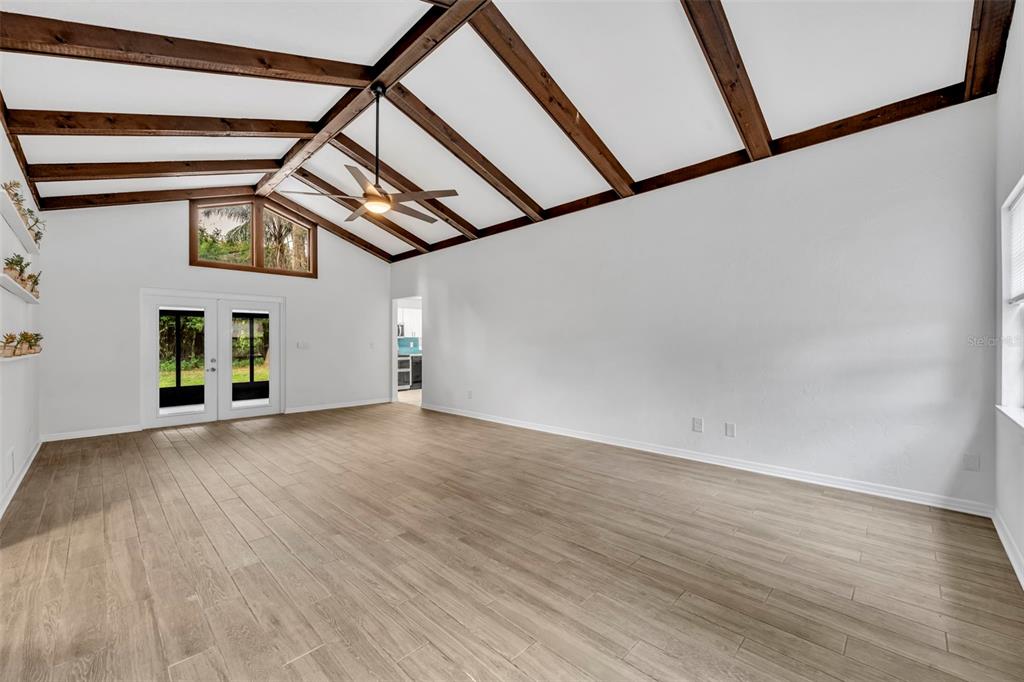 A spacious living room features vaulted ceilings with exposed wood beams and light wood flooring — 1240 W VOORHIS AVENUE, DELAND, FL