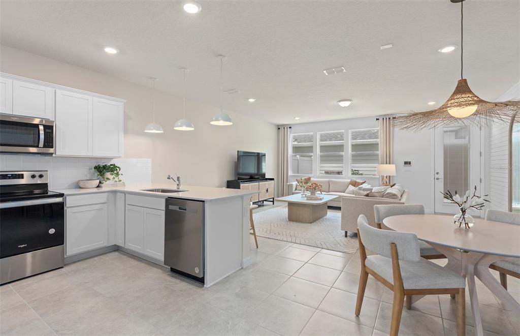 An open-concept kitchen and living area featuring white cabinets, stainless appliances, and tile flooring — 15508 PEACEFUL PINES ALLEY, CLERMONT, FL