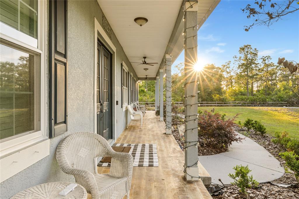 A covered front porch with white wicker chairs, wood-look flooring, and a view of trees — 19802 PEABODY STREET, ORLANDO, FL