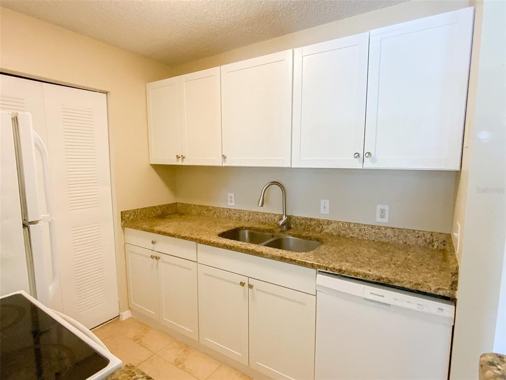 A kitchen features white cabinets, granite countertops, a double sink, and a white dishwasher — 455 ALT 19 S UNIT 53, PALM HARBOR, FL