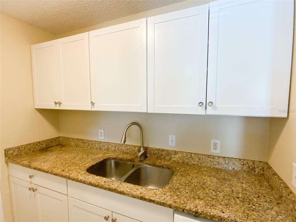 A kitchen features white shaker-style cabinets, a double-basin stainless steel sink, and granite countertops — 455 ALT 19 S UNIT 53, PALM HARBOR, FL