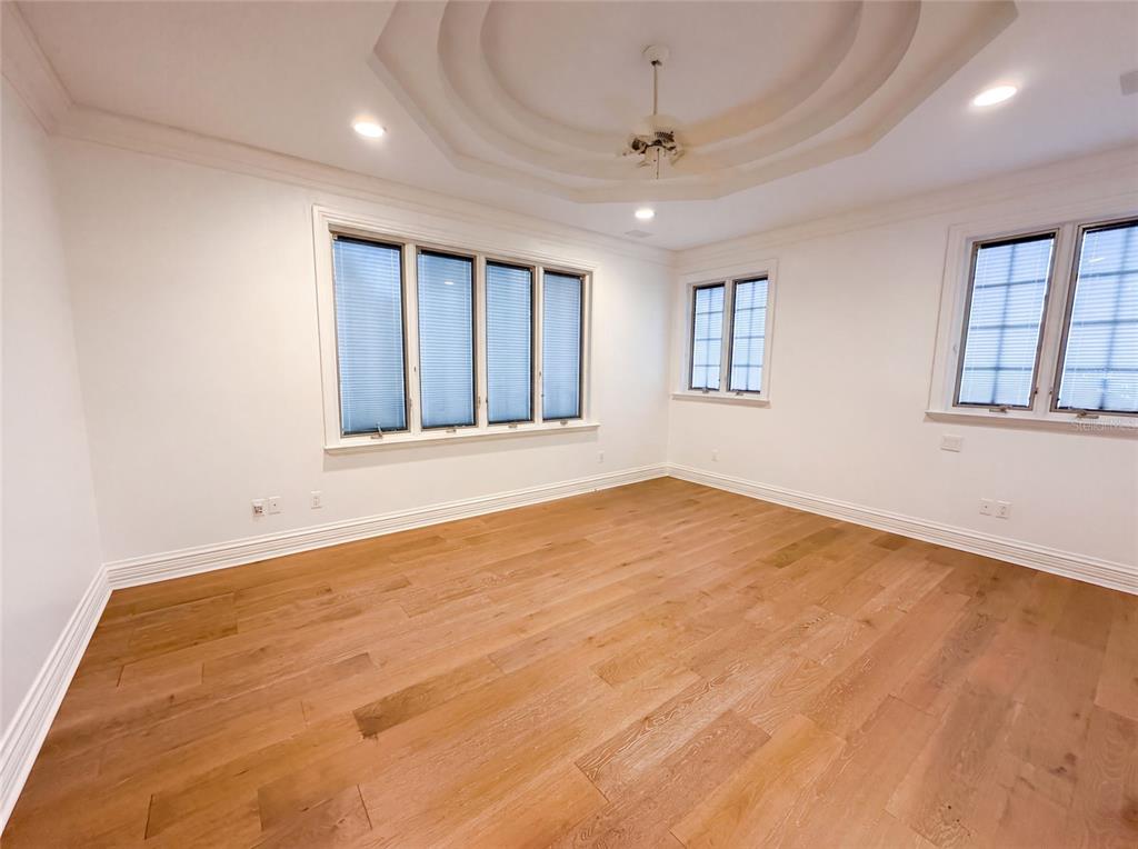 An empty room features light wood flooring, white walls, a tray ceiling, and multiple windows — 4407 W DALE AVENUE, TAMPA, FL