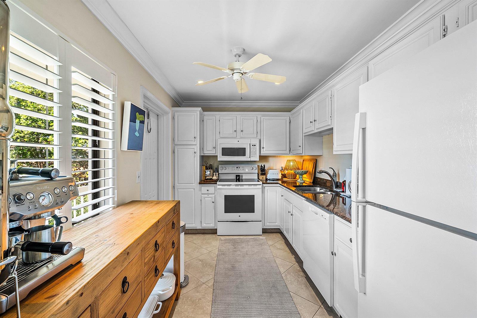 A galley kitchen features white cabinets, granite countertops, stainless steel appliances, and a wooden island — 4595 Kittiwake Court, Boynton Beach FL 33436, BOYNTON BEACH, FL