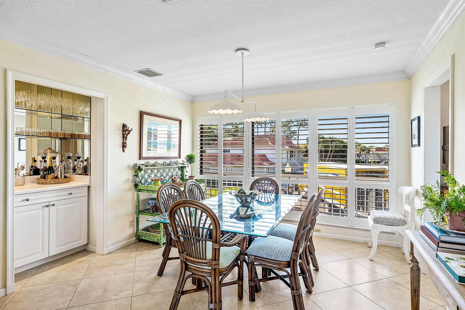 A dining room features a glass-topped table, rattan chairs, a wet bar, and plantation shutters — 4595 Kittiwake Court, Boynton Beach FL 33436, BOYNTON BEACH, FL