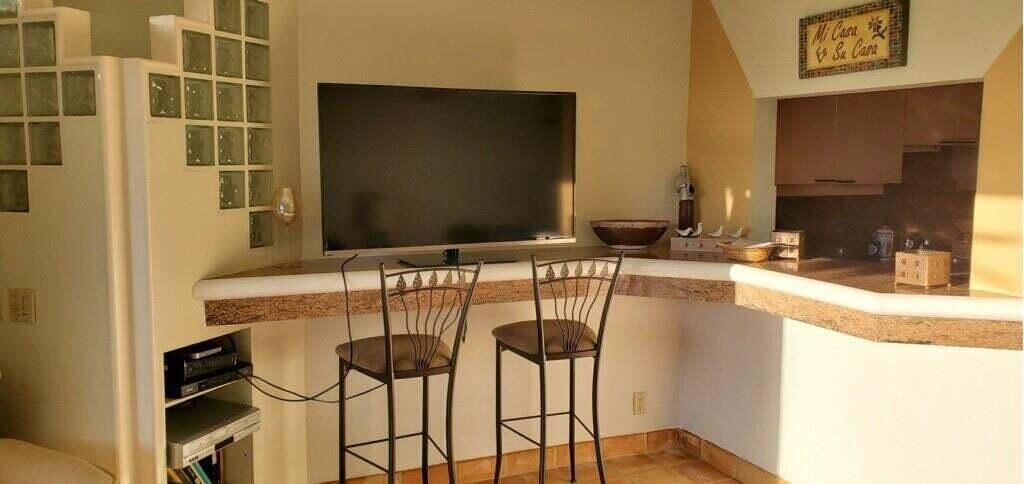 A kitchen breakfast bar with two metal stools sits below a wall-mounted television — 55 NE Spanish Trail # 2040, Boca Raton FL 33432, BOCA RATON, FL
