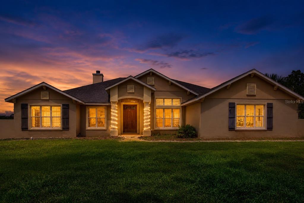 A single-story house with a tan stucco exterior and dark shutters at dusk — 1098 NW 165TH COURT ROAD, DUNNELLON, FL