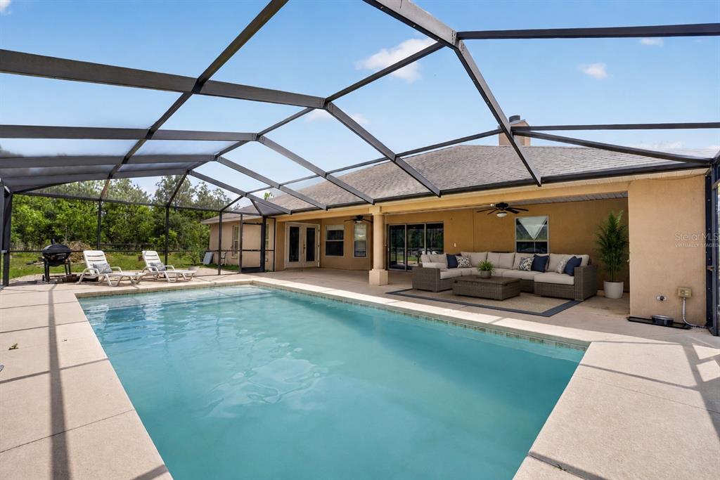 A swimming pool sits on a patio enclosed by a screen cage behind a house — 1098 NW 165TH COURT ROAD, DUNNELLON, FL