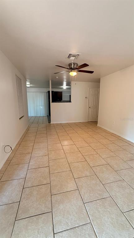 A living room with light-colored tile flooring, a ceiling fan, and a view of the kitchen — 1604 WOODLYN DRIVE, LEESBURG, FL