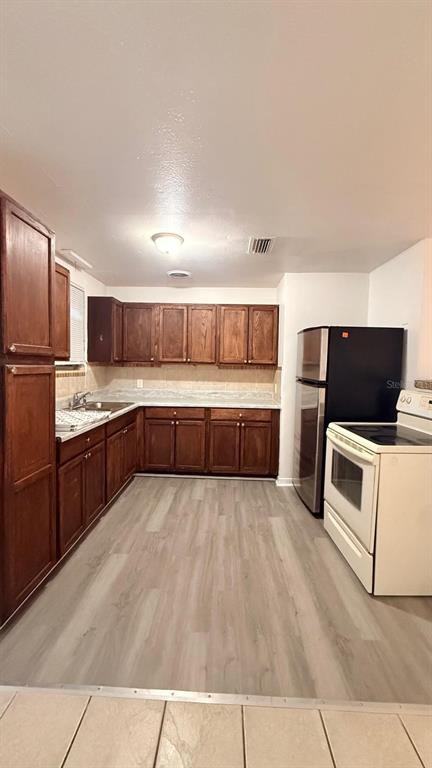 A kitchen with wood cabinets, light countertops, stainless steel appliances, and light-colored wood-look flooring — 1604 WOODLYN DRIVE, LEESBURG, FL