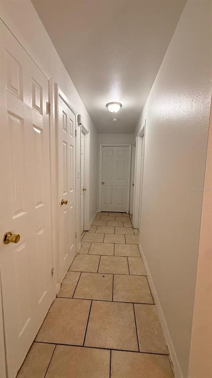 A narrow hallway with light-colored tile flooring, white walls, and several white interior doors — 1604 WOODLYN DRIVE, LEESBURG, FL