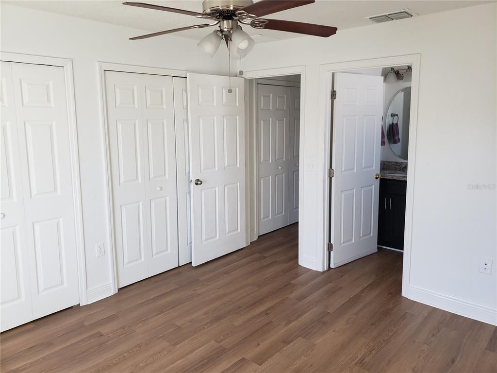 A bedroom features wood-look flooring, a ceiling fan, multiple white doors, and an attached bathroom — 100 SWEET PEA COURT, POINCIANA, FL