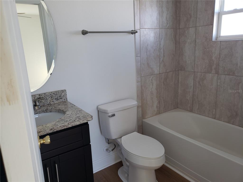 A bathroom features a dark vanity with a granite countertop, a toilet, and a tiled tub — 100 SWEET PEA COURT, POINCIANA, FL