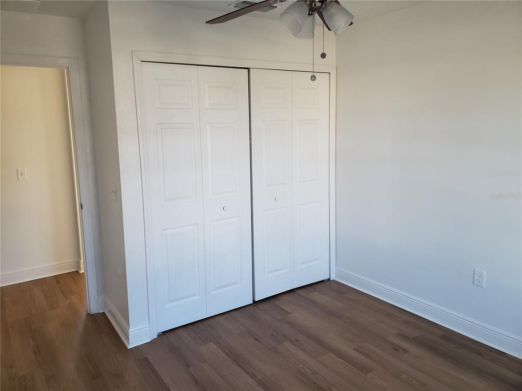 A bedroom features white bi-fold closet doors, a ceiling fan, and wood-look flooring — 100 SWEET PEA COURT, POINCIANA, FL