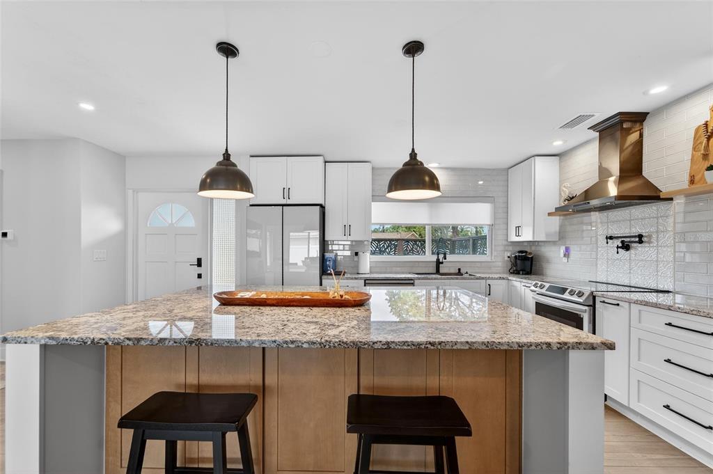 A kitchen features a granite-topped island, white cabinetry, stainless steel appliances, and two pendant lights — 2 79TH STREET S, ST PETERSBURG, FL