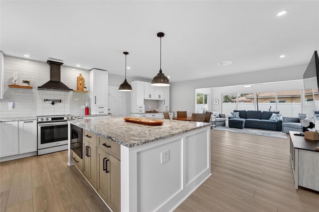 A kitchen with a granite-topped island and white cabinets opens into a living room area — 2 79TH STREET S, ST PETERSBURG, FL