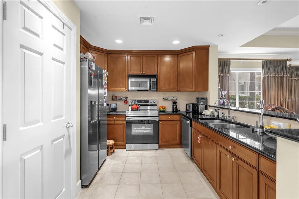 A kitchen features wood cabinets, stainless steel appliances, black granite countertops, and light tile flooring — 1364 CENTRE COURT RIDGE DRIVE UNIT 101, REUNION, FL