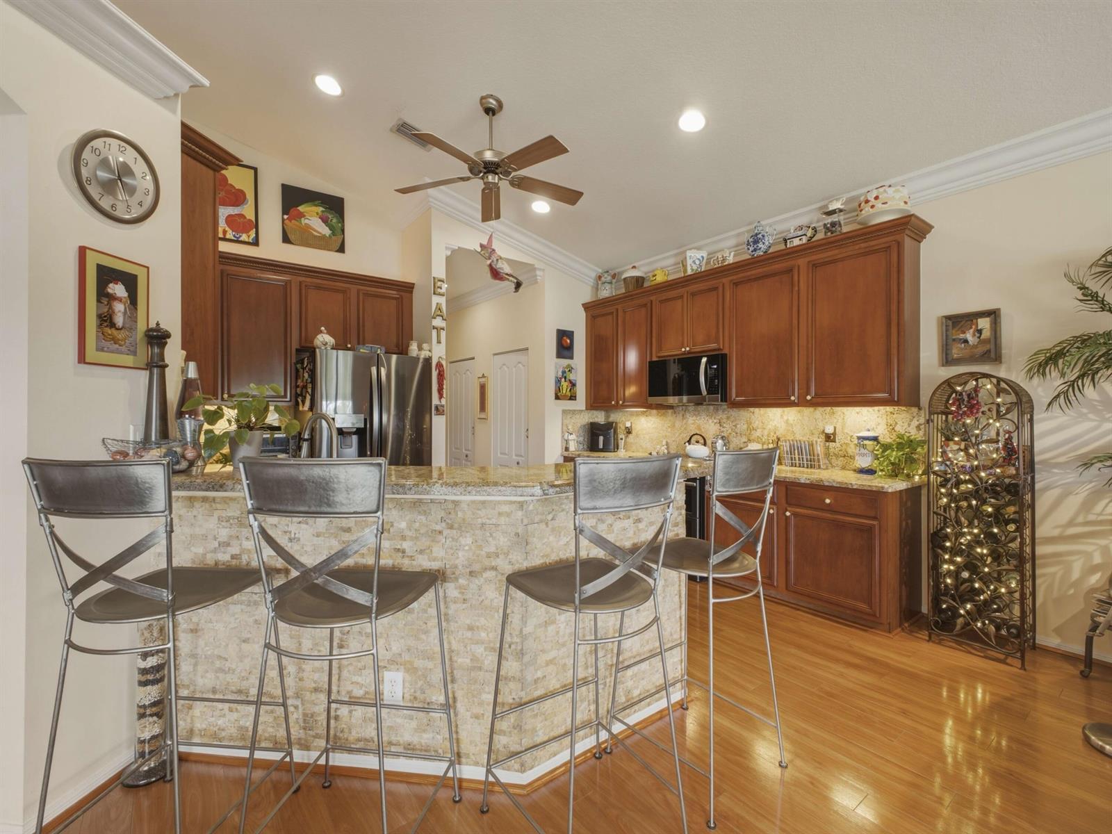 A kitchen features wood cabinets, granite countertops, a stone-tiled breakfast bar, and four metal stools — 8328 GRAND MESSINA Circle, Boynton Beach FL 33472, BOYNTON BEACH, FL