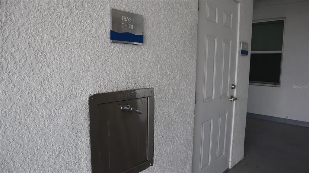 A white wall features a metal trash chute door and a nearby apartment entrance door — 3120 PARADOX CIRCLE UNIT 205, KISSIMMEE, FL