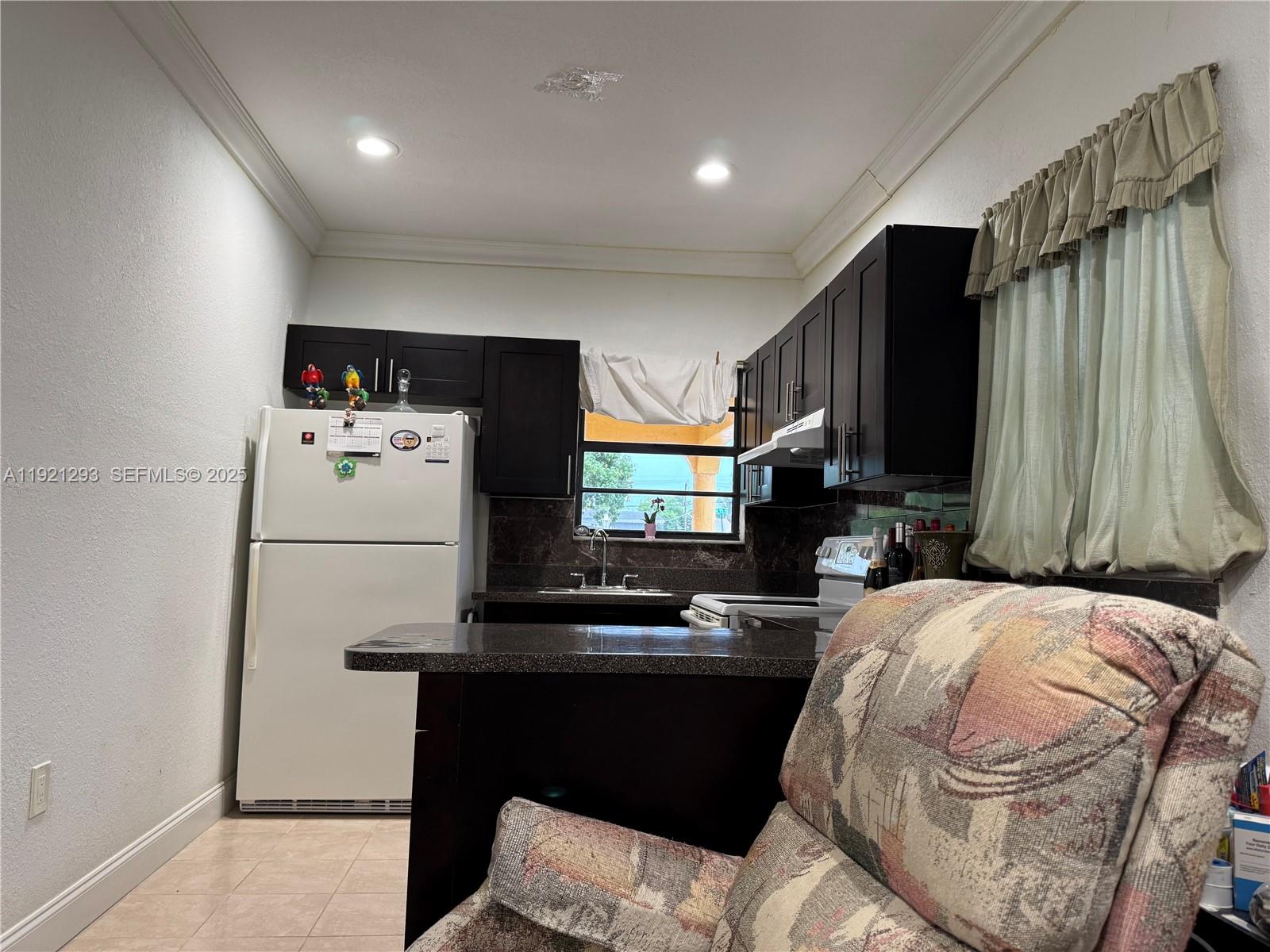 A kitchen features dark wood cabinets, granite countertops, a white refrigerator, and a patterned armchair — 3041 NW 95th Ter, Miami FL 33147, MIAMI, FL