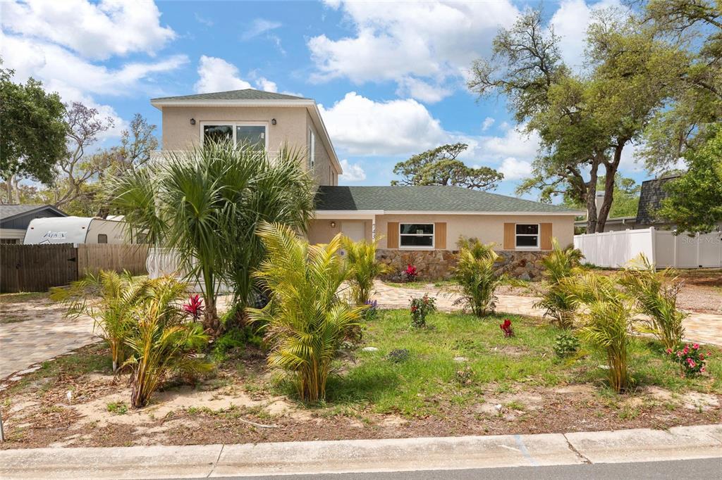 A two-story house with a stone facade, green roof, and palm trees in the front yard — 743 BAYSHORE DRIVE, TARPON SPRINGS, FL