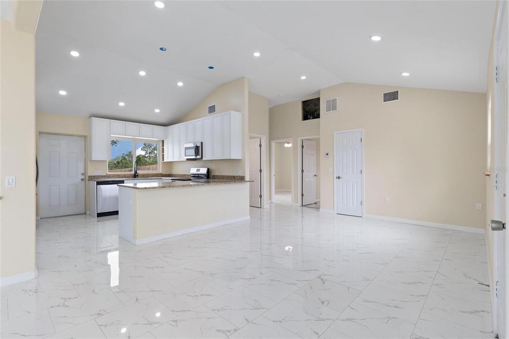 An open-concept kitchen and living area features white cabinets, granite countertops, and marble-look tile flooring — 743 BAYSHORE DRIVE, TARPON SPRINGS, FL