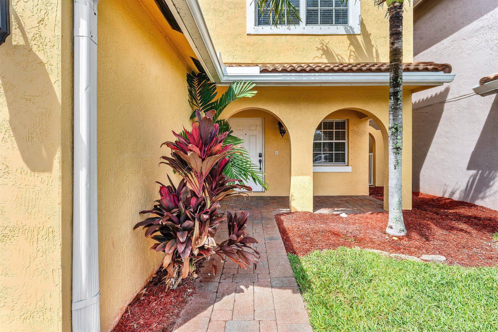 A yellow stucco house exterior features an arched entryway, a brick walkway, and tropical landscaping — 3260 Commodore Court, West Palm Beach FL 33411, WEST PALM BEACH, FL